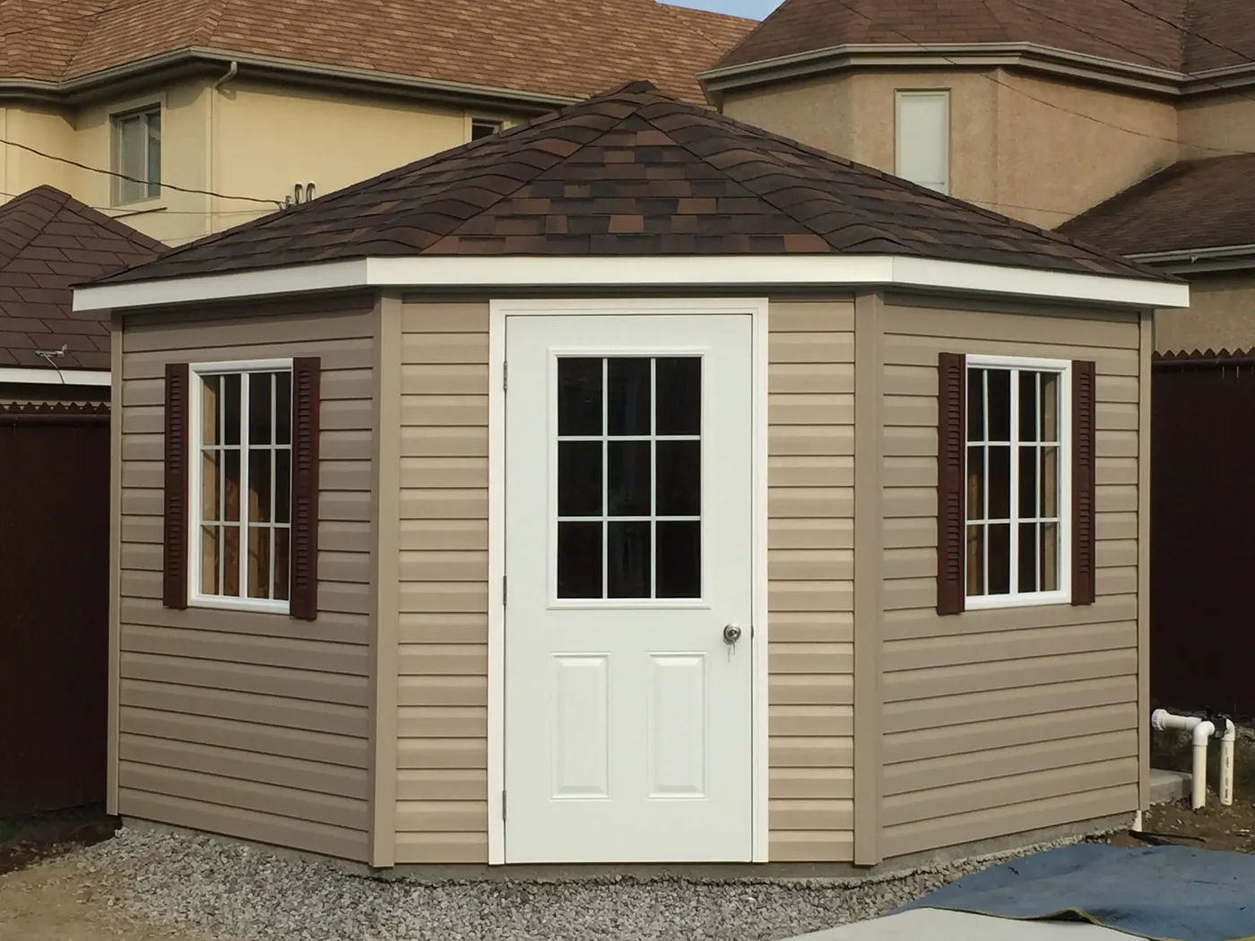 Cabanon beige à façade en angle, porte vitrée blanche et fenêtres latérales.