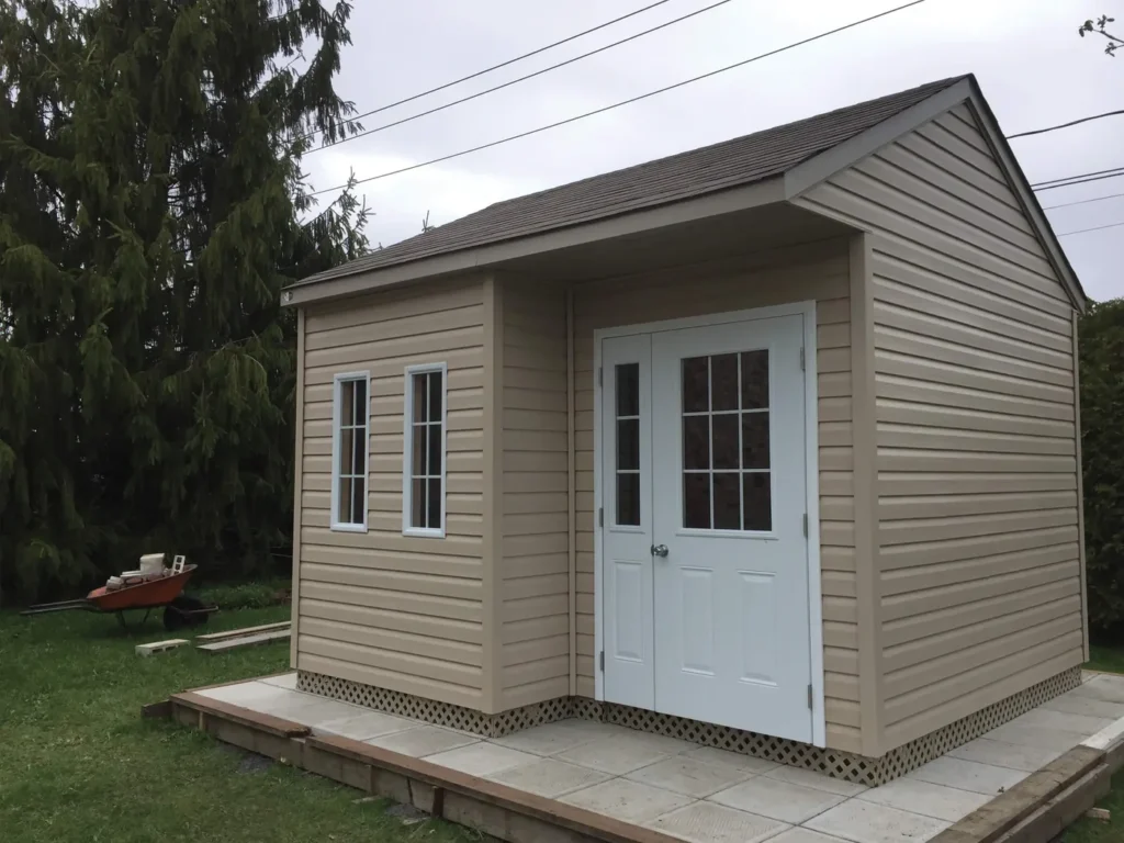 Cabanon beige à porte vitrée blanche, photographié avec sa base et son espace d’approche.