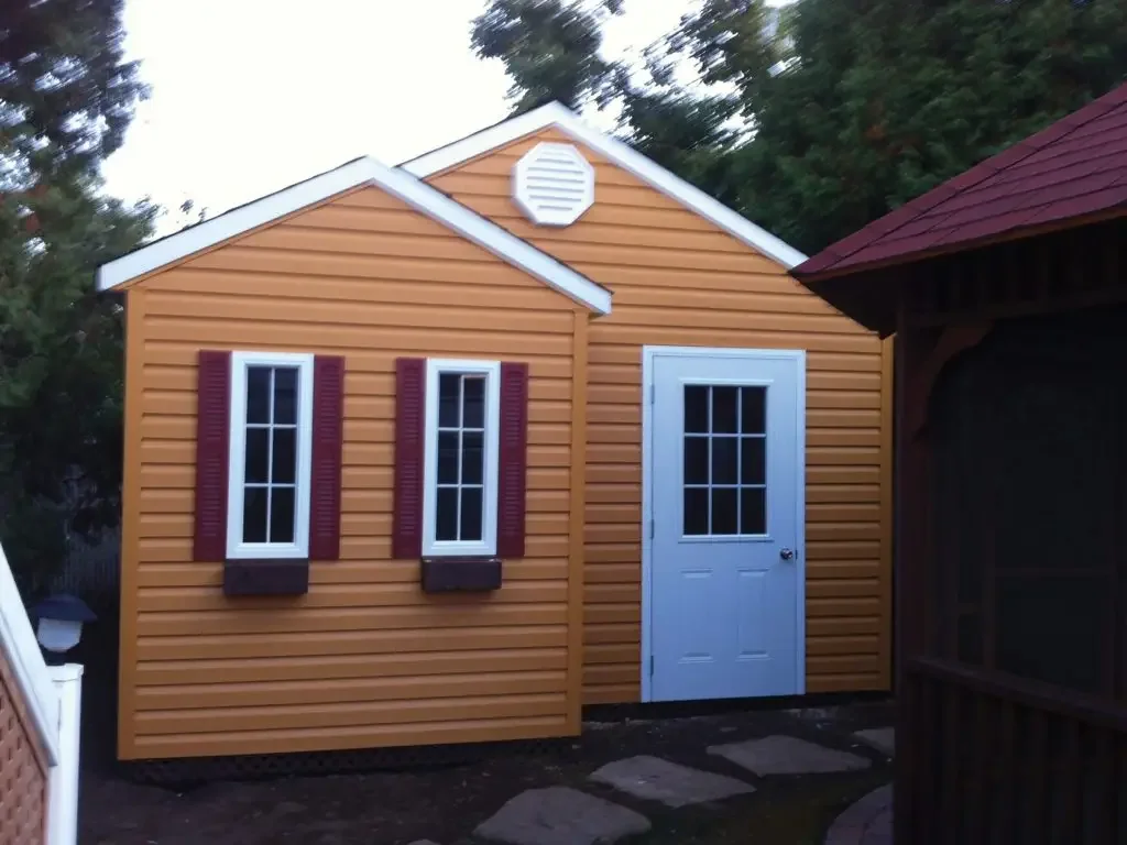 Cabanon orangé à deux pignons, porte vitrée et fenêtres à volets.